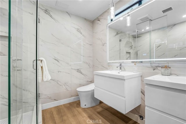 bathroom with tile walls, a marble finish shower, toilet, vanity, and wood finished floors