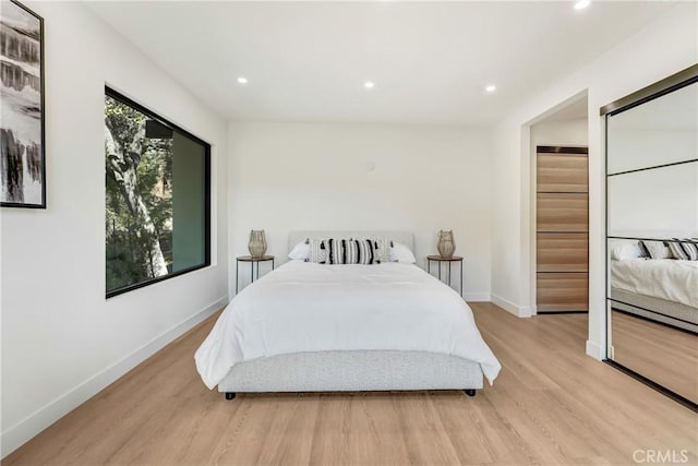 bedroom with light wood finished floors, recessed lighting, a walk in closet, and baseboards