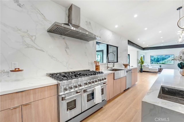 kitchen with a sink, wall chimney range hood, appliances with stainless steel finishes, light brown cabinetry, and modern cabinets