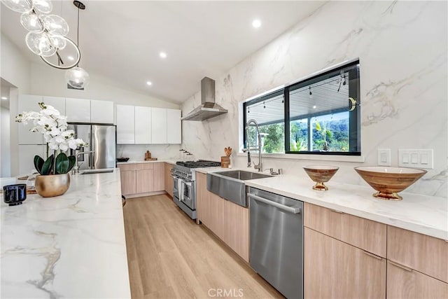 kitchen with a sink, appliances with stainless steel finishes, light stone countertops, wall chimney exhaust hood, and modern cabinets