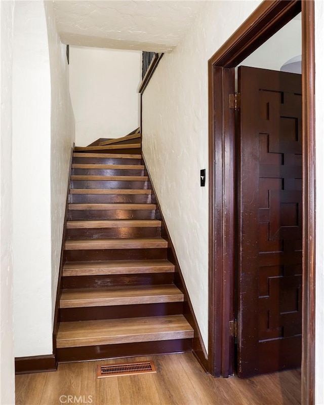 staircase featuring baseboards, visible vents, wood finished floors, and a textured wall