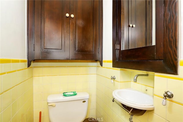 half bathroom featuring tile walls, a sink, and toilet