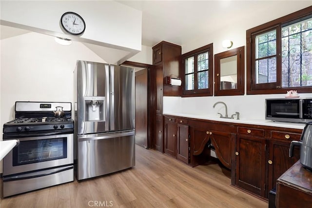 kitchen with light countertops, dark brown cabinetry, a sink, light wood-style flooring, and stainless steel appliances