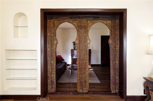 interior details with baseboards, arched walkways, wood finished floors, and built in shelves