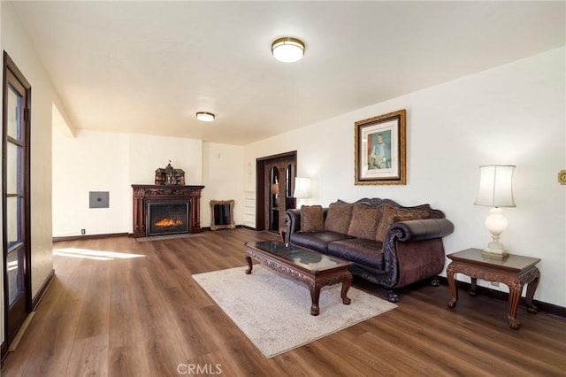living area with baseboards, a warm lit fireplace, and dark wood-type flooring