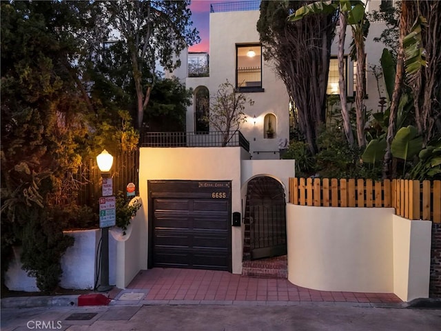 view of front of property with a balcony, fence, a gate, and stucco siding