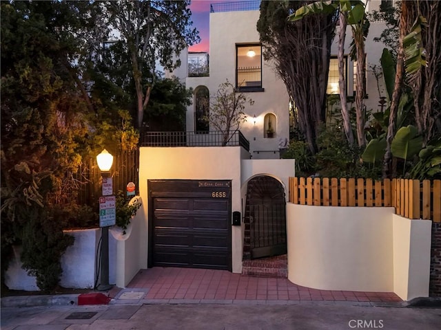 view of front of house with a gate, stucco siding, fence, a balcony, and decorative driveway