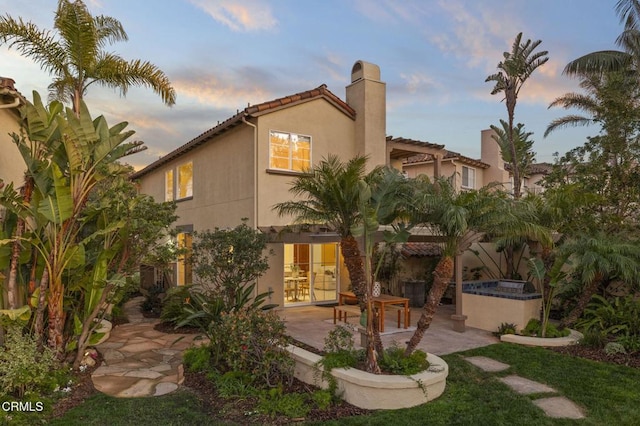 back of house at dusk featuring a patio area and stucco siding