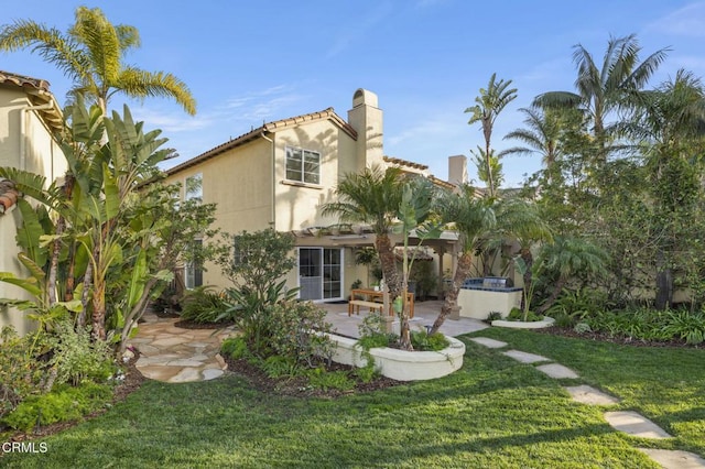 rear view of house featuring a patio area, a yard, a chimney, and stucco siding