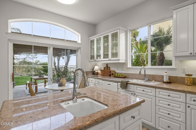 kitchen featuring a sink, white cabinetry, light stone countertops, dishwasher, and glass insert cabinets