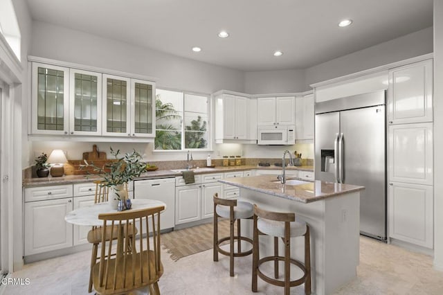 kitchen featuring glass insert cabinets, a kitchen island with sink, white cabinets, white appliances, and a kitchen bar