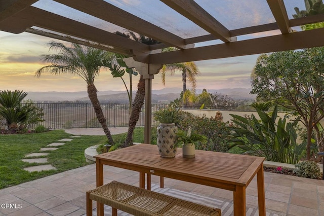 patio terrace at dusk featuring a yard, a fenced backyard, a mountain view, and a pergola