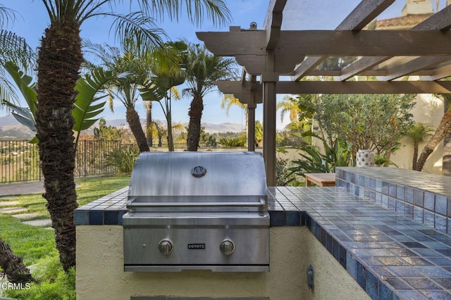 view of patio with an outdoor kitchen, area for grilling, a mountain view, fence, and a pergola