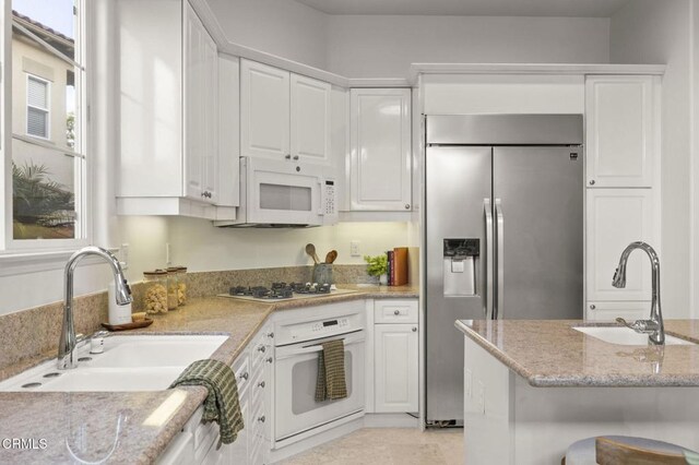 kitchen with white appliances, white cabinetry, a sink, and light stone countertops