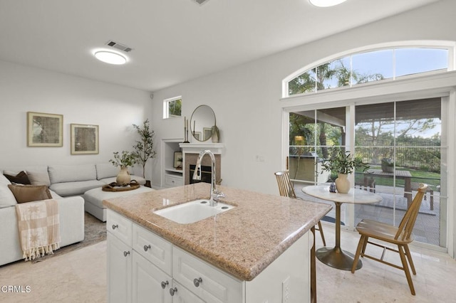 kitchen featuring visible vents, white cabinets, a glass covered fireplace, a kitchen island with sink, and a sink