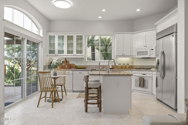 kitchen with a kitchen island, a kitchen breakfast bar, white cabinets, appliances with stainless steel finishes, and glass insert cabinets