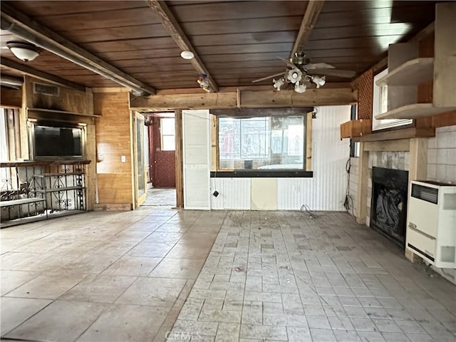 unfurnished living room featuring wood walls, a ceiling fan, heating unit, wooden ceiling, and beamed ceiling
