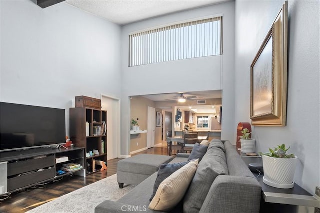 living room featuring baseboards, visible vents, dark wood finished floors, a ceiling fan, and a towering ceiling