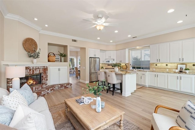 living room with visible vents, light wood-style flooring, ornamental molding, a fireplace, and recessed lighting