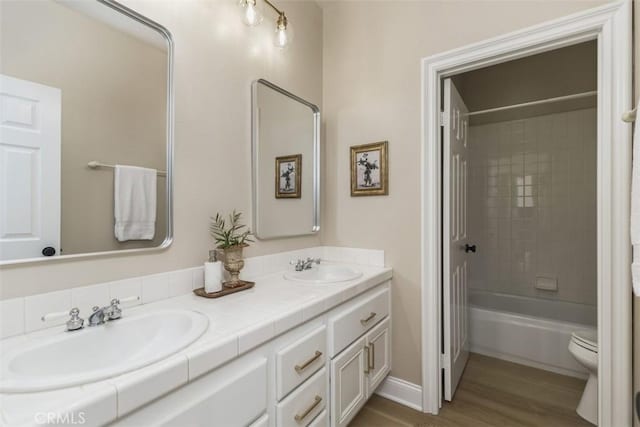 bathroom featuring double vanity, wood finished floors, a sink, and toilet