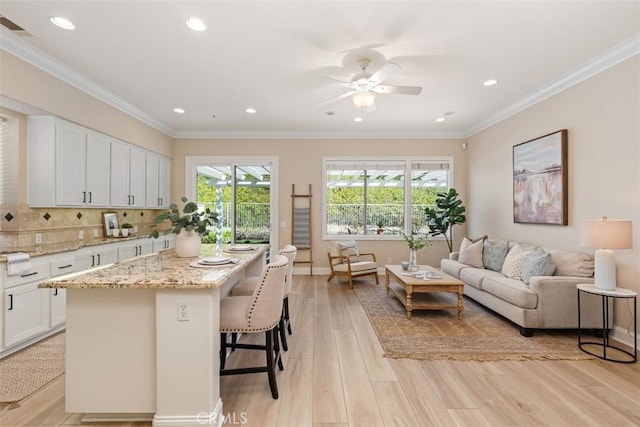 kitchen featuring light wood-type flooring, ornamental molding, white cabinets, and light stone counters