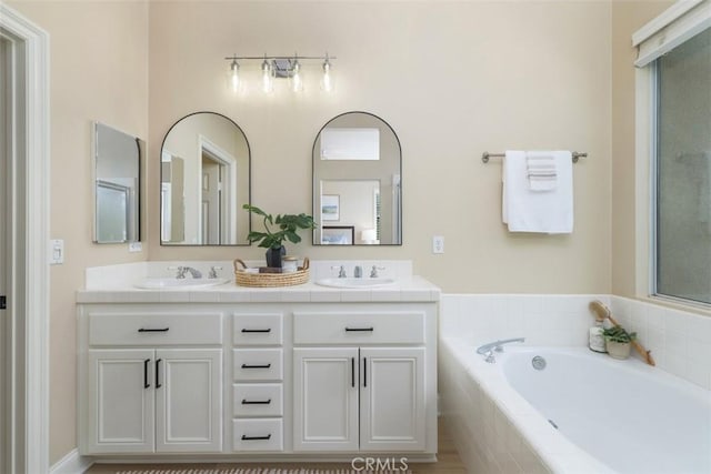 bathroom with double vanity, a garden tub, and a sink