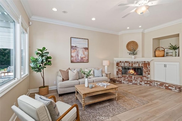 living room featuring a brick fireplace, crown molding, a wealth of natural light, and wood finished floors