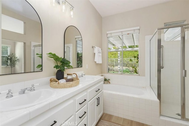 full bath with a bath, a stall shower, double vanity, and a sink