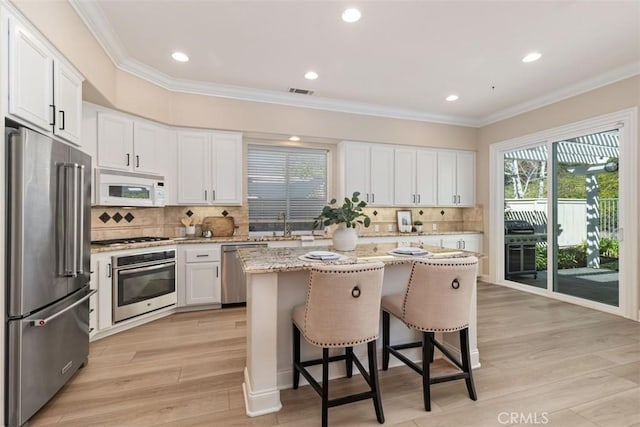 kitchen featuring a breakfast bar, a center island, stainless steel appliances, crown molding, and light wood-style floors