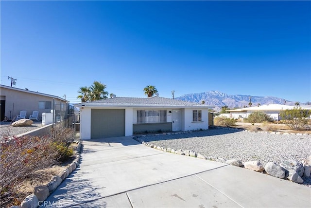 single story home with concrete driveway, an attached garage, fence, a mountain view, and stucco siding