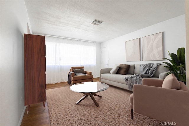 living room featuring visible vents, a textured ceiling, baseboards, and wood finished floors