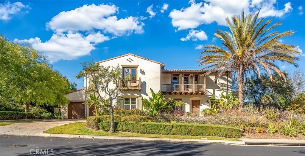 mediterranean / spanish house with concrete driveway, a tile roof, a balcony, and stucco siding