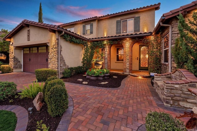 mediterranean / spanish-style house with stone siding, an attached garage, and stucco siding