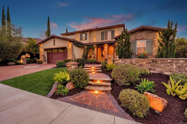 mediterranean / spanish house featuring decorative driveway, stucco siding, a garage, stone siding, and a tiled roof