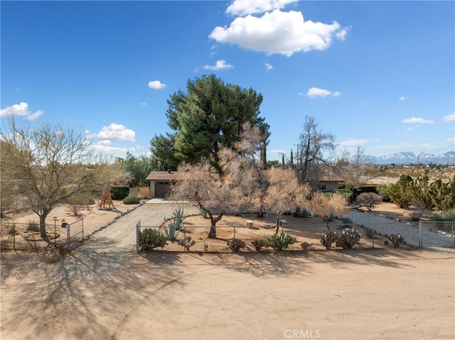 view of yard with driveway, a rural view, an attached garage, fence, and a mountain view