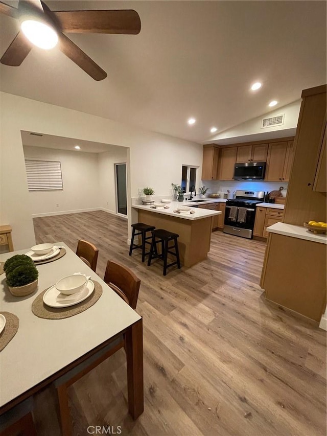 kitchen featuring light countertops, visible vents, appliances with stainless steel finishes, brown cabinetry, and a kitchen bar