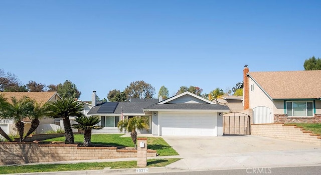 view of front of property with driveway, a garage, solar panels, a gate, and stucco siding