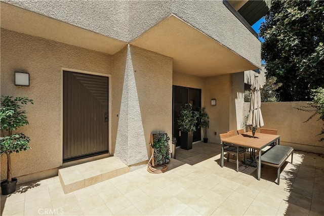 doorway to property with outdoor dining space, a patio, fence, and stucco siding