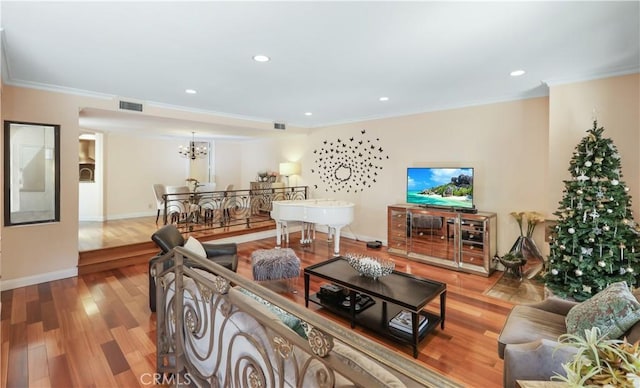 living area with a notable chandelier, wood finished floors, visible vents, baseboards, and crown molding