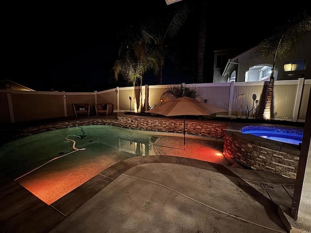 pool at night with a fenced backyard, a patio, and an in ground hot tub