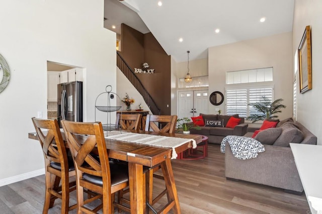 dining area with recessed lighting, wood finished floors, a towering ceiling, baseboards, and stairway