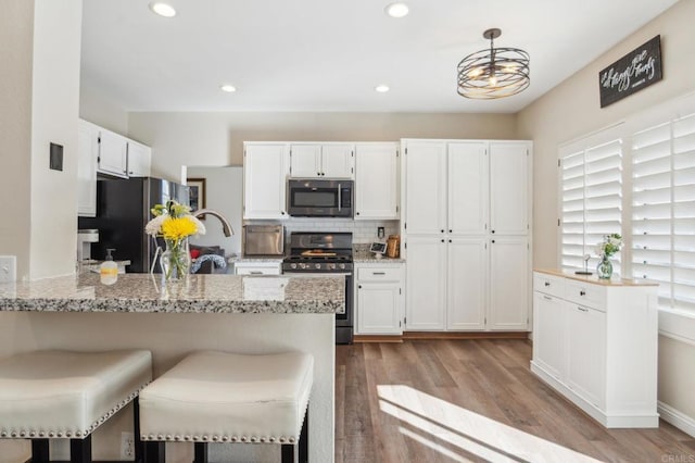 kitchen with light stone counters, decorative light fixtures, appliances with stainless steel finishes, white cabinetry, and light wood-type flooring