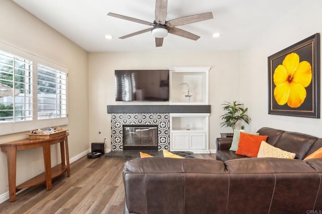 living area featuring baseboards, a ceiling fan, a tile fireplace, wood finished floors, and recessed lighting