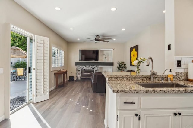 kitchen featuring a fireplace, a sink, white cabinets, light wood-type flooring, and light stone countertops