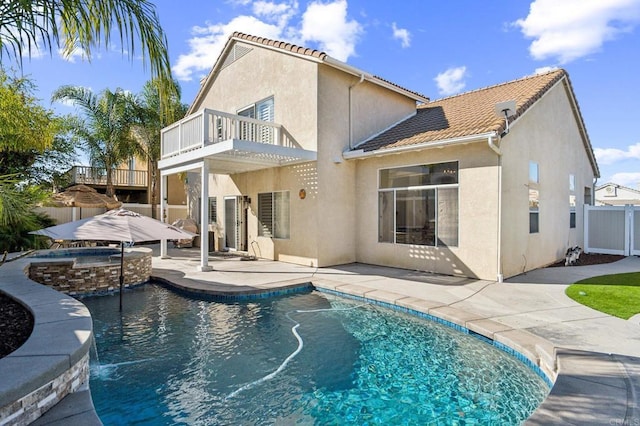 back of house with a balcony, a tile roof, fence, and stucco siding