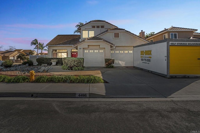 view of front facade featuring concrete driveway, a tile roof, an attached garage, and stucco siding