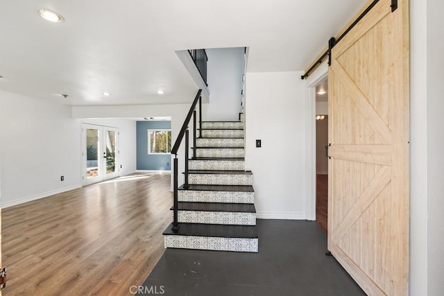 stairway with a barn door, baseboards, wood finished floors, and french doors