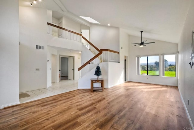 unfurnished living room featuring stairway, a skylight, visible vents, and light wood-style flooring