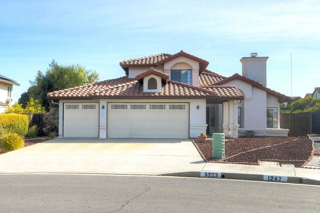 mediterranean / spanish home with an attached garage, fence, concrete driveway, a tiled roof, and stucco siding