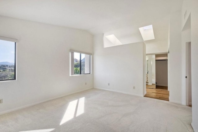 unfurnished bedroom featuring light carpet, vaulted ceiling with skylight, and baseboards